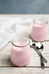 Glass jars with creamy yogurt served on white wooden table. Space for text