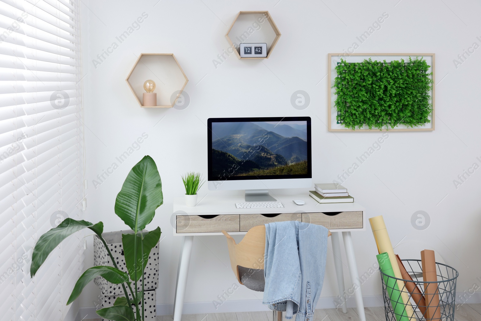 Photo of Green artificial plant wall panel and desk with computer in light room. Interior design