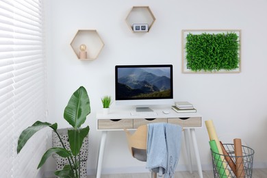 Green artificial plant wall panel and desk with computer in light room. Interior design