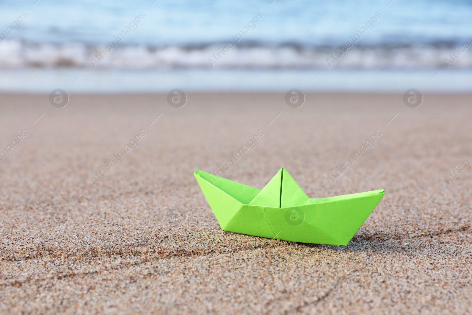 Photo of Light green paper boat near sea on sandy beach, space for text