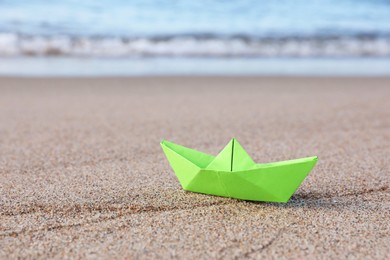 Light green paper boat near sea on sandy beach, space for text