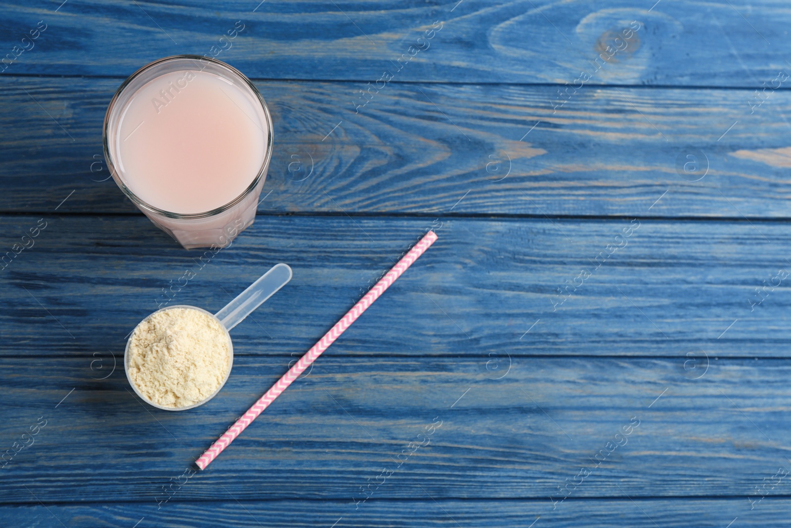 Photo of Protein shake, powder and straw on blue wooden table, flat lay. Space for text