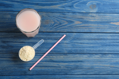 Protein shake, powder and straw on blue wooden table, flat lay. Space for text