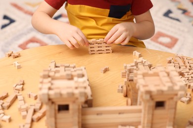 Photo of Little boy playing with wooden construction set at table indoors, closeup. Child's toy