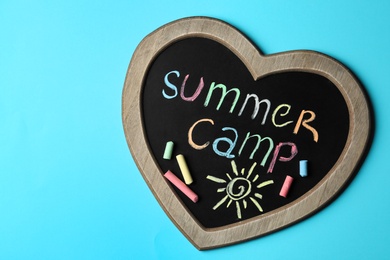 Heart shaped blackboard with text SUMMER CAMP, drawing and chalk sticks on color background, top view. Space for design