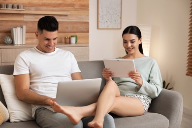 Photo of Happy couple in pyjamas with gadgets spending time together on sofa at home