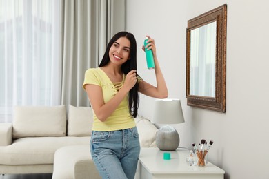 Woman applying dry shampoo onto her hair near mirror at home