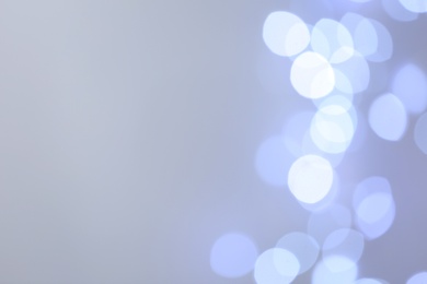 Blurred view of beautiful lights on light grey background, space for text