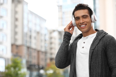 Photo of Handsome young African-American man with headphones listening to music on city street. Space for text