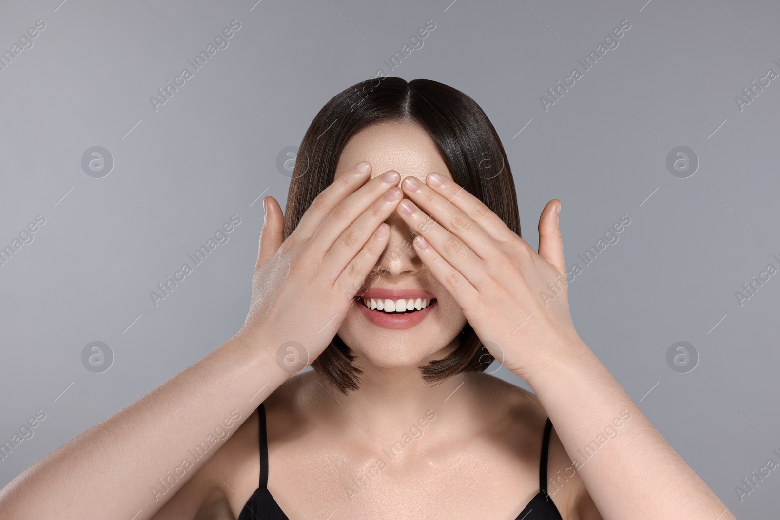 Image of Portrait of pretty young woman with brown hair smiling and closing her eyes on grey background