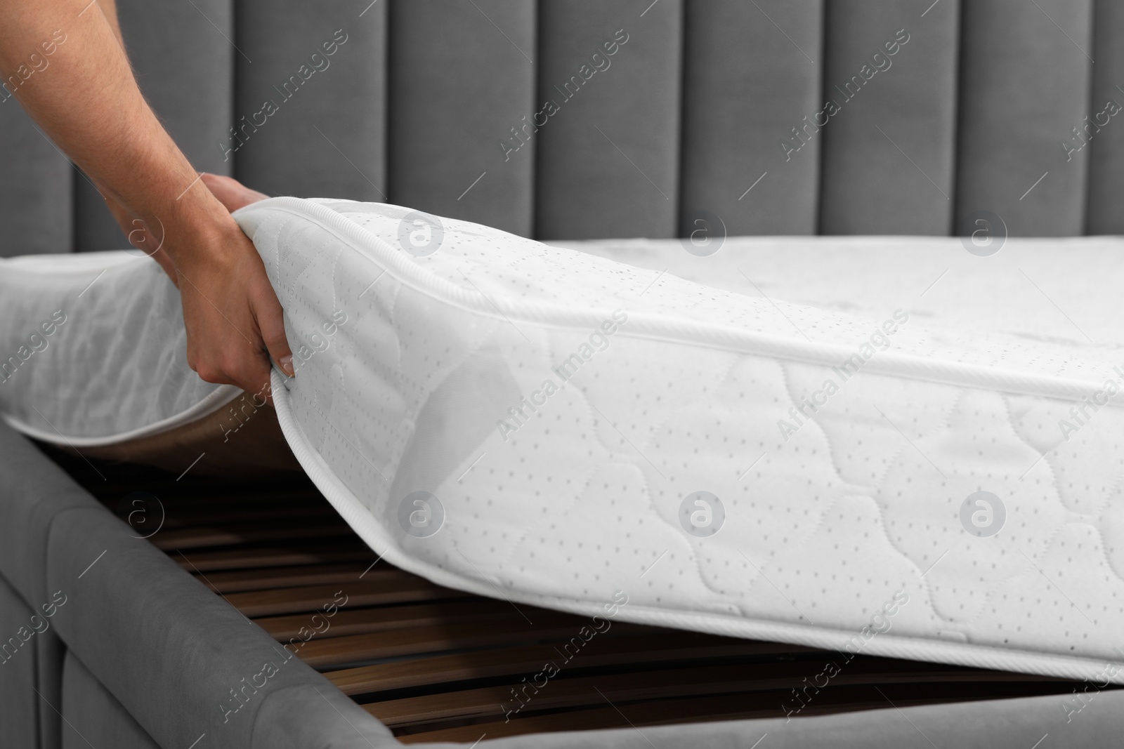 Photo of Man putting soft mattress on bed, closeup