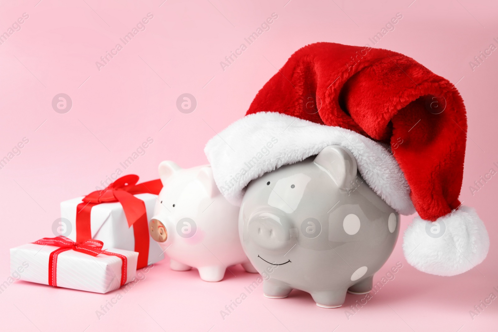 Photo of Piggy banks with Santa hat and gift boxes on pink background