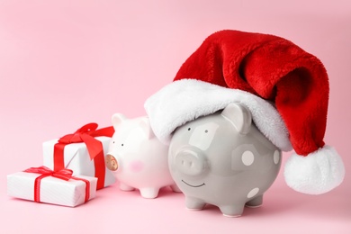 Photo of Piggy banks with Santa hat and gift boxes on pink background