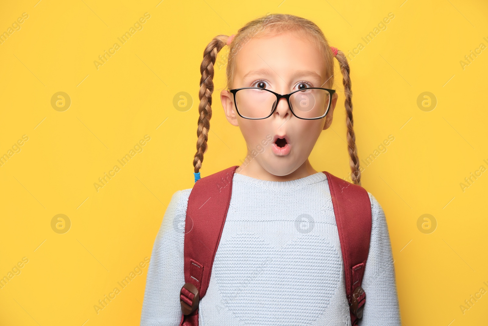 Photo of Cute little girl with backpack wearing glasses on yellow background