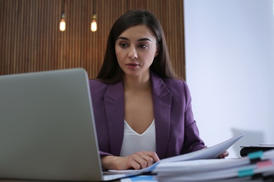 Businesswoman working with laptop and documents at table in office