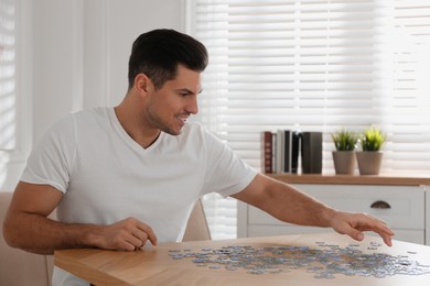 Photo of Man playing with puzzles at wooden table indoors