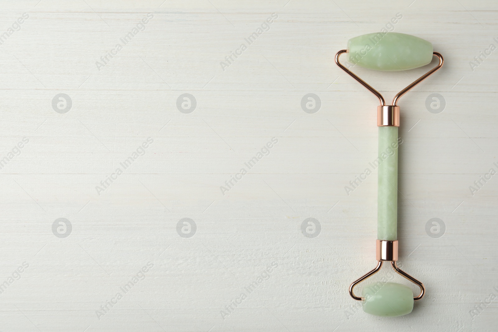 Photo of Natural jade face roller on white wooden background, top view. Space for text