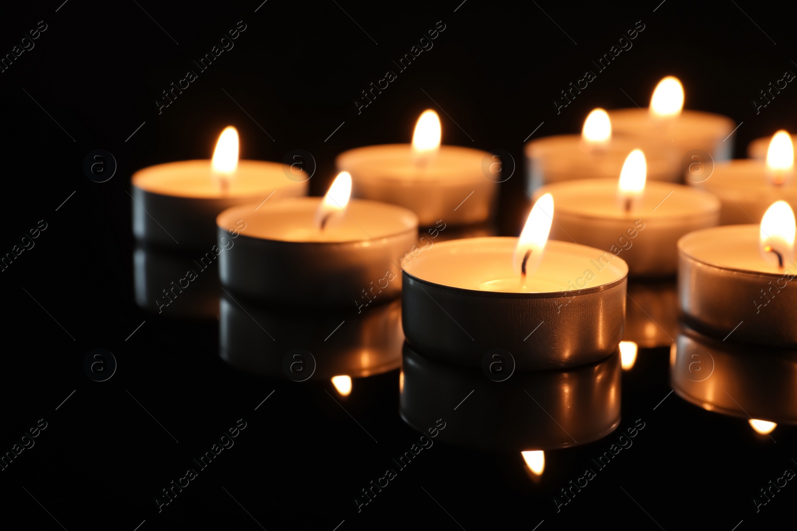 Photo of Wax candles burning on table in darkness, closeup