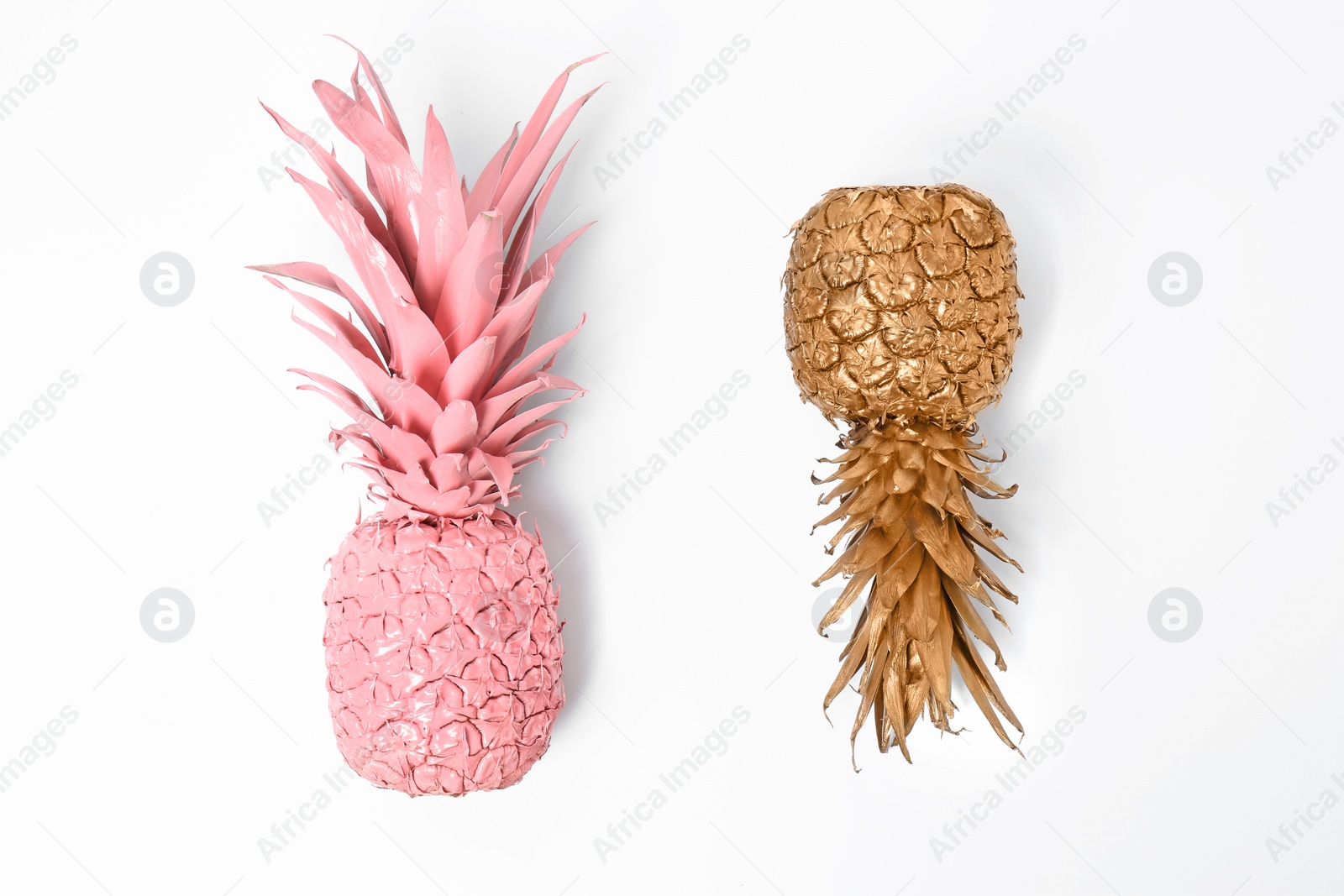 Photo of Shiny stylish gold and pink pineapples on white background, top view