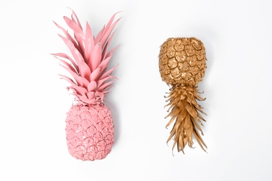 Photo of Shiny stylish gold and pink pineapples on white background, top view