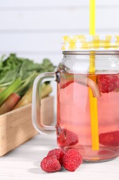 Mason jar of tasty rhubarb cocktail with raspberry on white wooden table, closeup