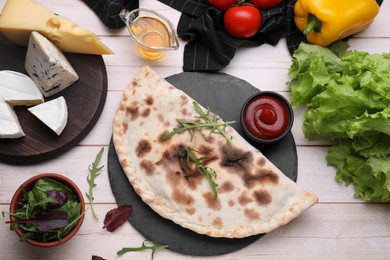 Photo of Delicious calzone and products on light wooden table, flat lay