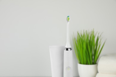 Photo of Electric toothbrush and tube with paste on light background