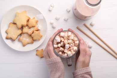 Woman drinking aromatic hot chocolate with marshmallows and cocoa powder at white wooden table, top view