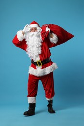 Photo of Santa Claus with bag of Christmas gifts posing on light blue background