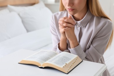 Photo of Religious young woman with Bible praying in bedroom, closeup