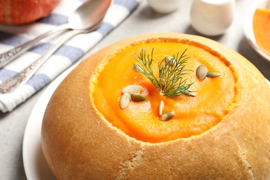 Photo of Tasty pumpkin soup served in bread on table, closeup