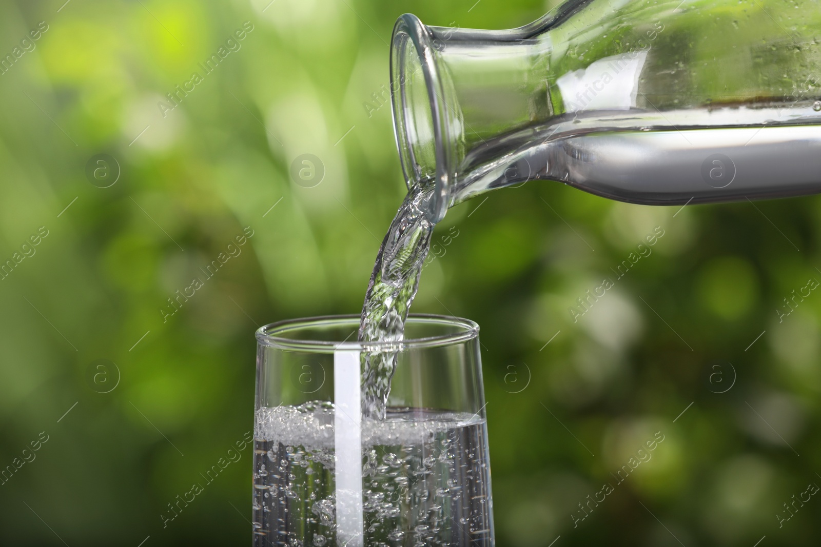 Photo of Pouring water from bottle into glass on blurred green background, closeup