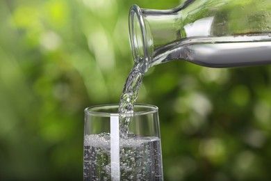Pouring water from bottle into glass on blurred green background, closeup