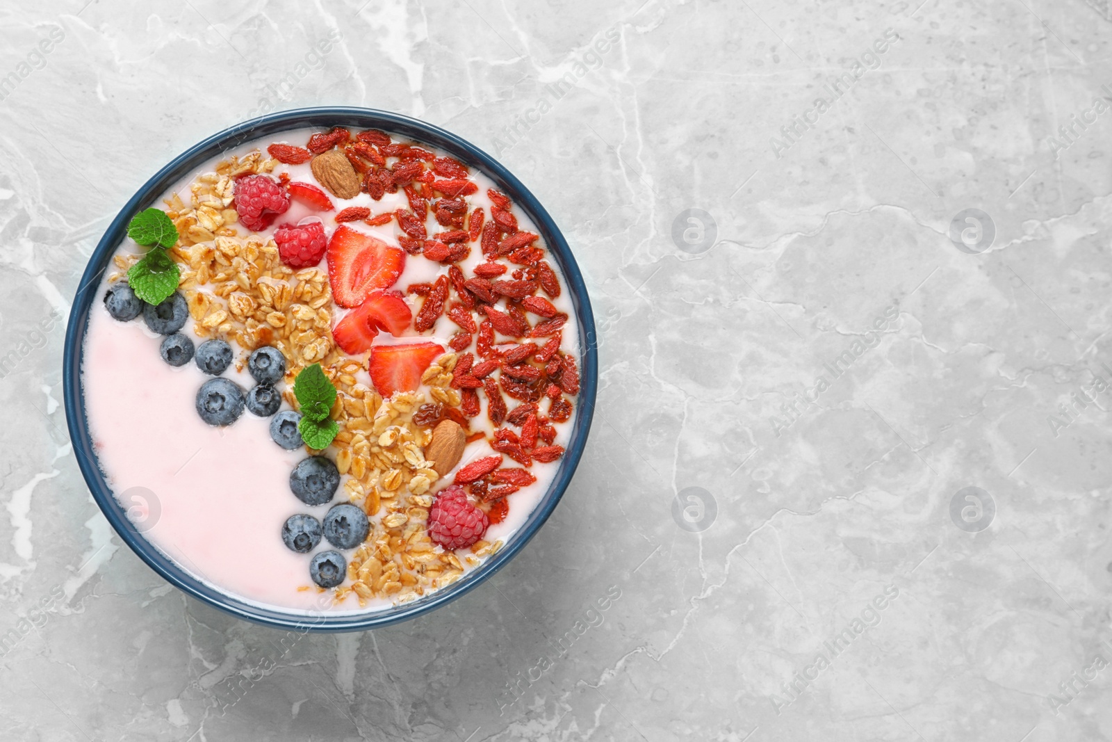 Photo of Smoothie bowl with goji berries on grey table, top view. Space for text