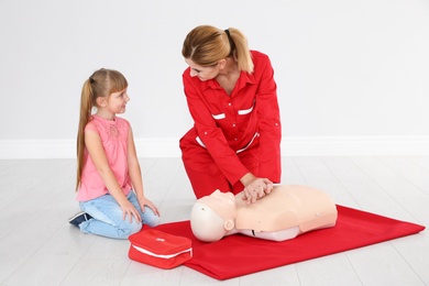 Instructor with little girl practicing first aid on mannequin indoors