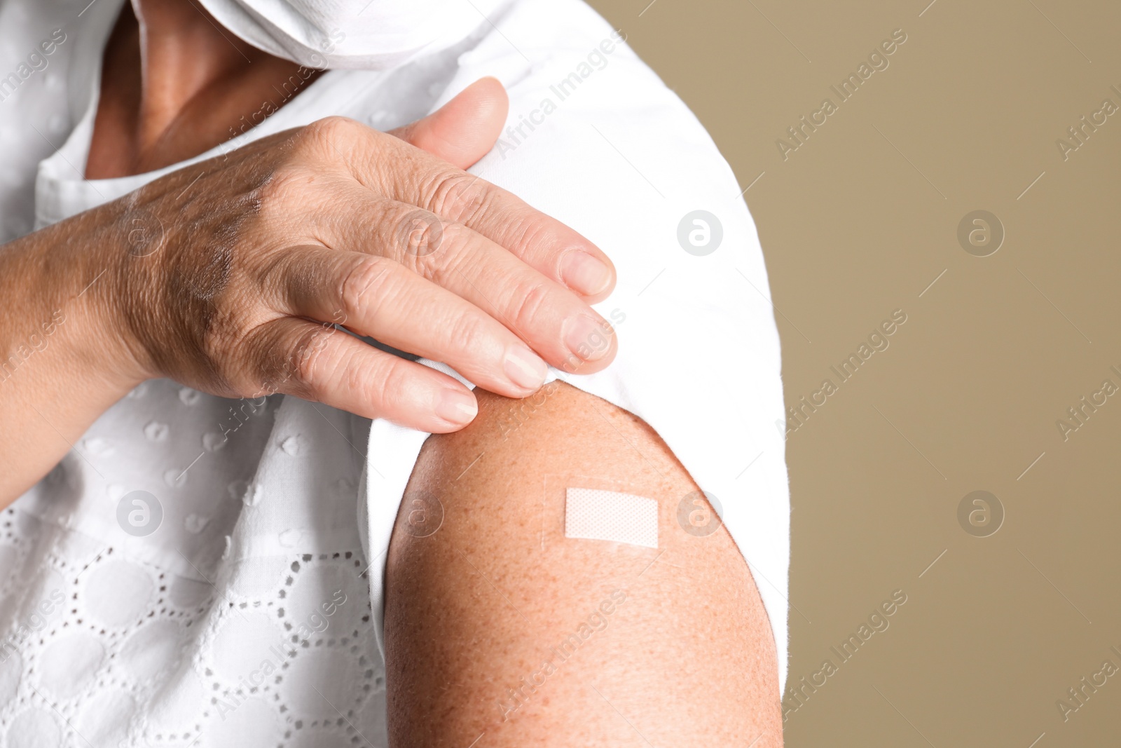 Photo of Mature woman in protective mask showing arm with bandage after vaccination on beige background, closeup