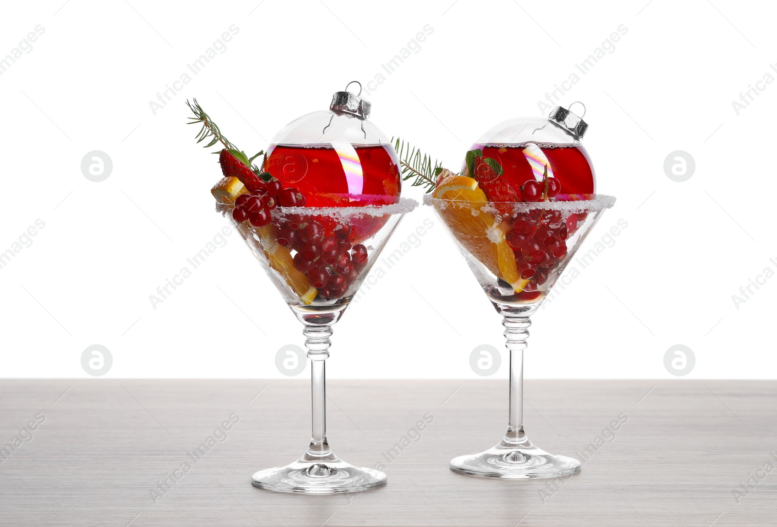 Photo of Creative presentation of Christmas Sangria cocktail in baubles and glasses on light wooden table against white background