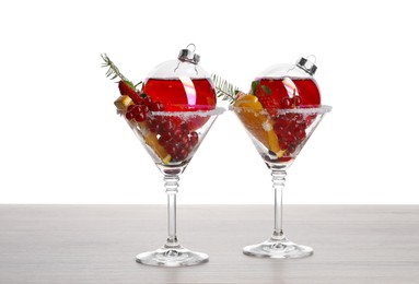 Photo of Creative presentation of Christmas Sangria cocktail in baubles and glasses on light wooden table against white background