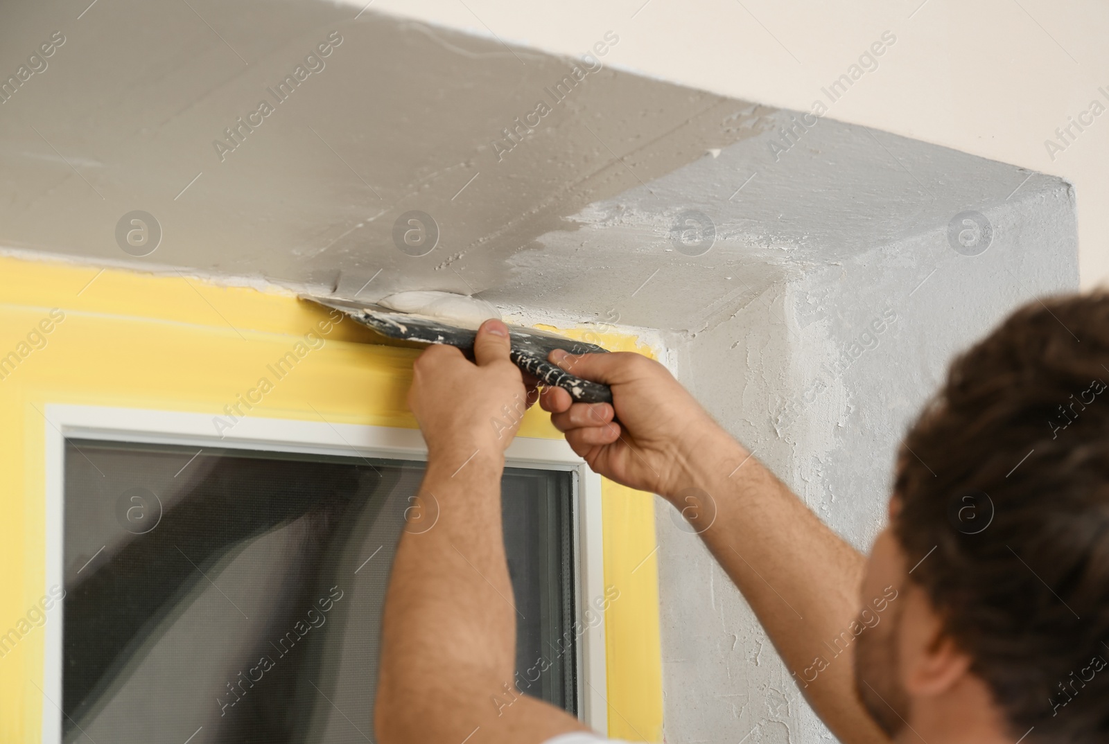 Photo of Man plastering window area with putty knife indoors, closeup. Interior repair