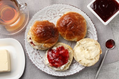 Photo of Freshly baked soda water scones with cranberry jam, butter and cup of tea on light grey table, flat lay