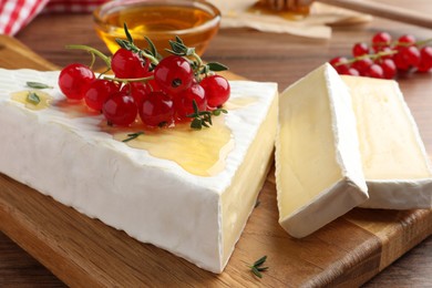 Photo of Brie cheese served with red currants and honey on wooden table, closeup