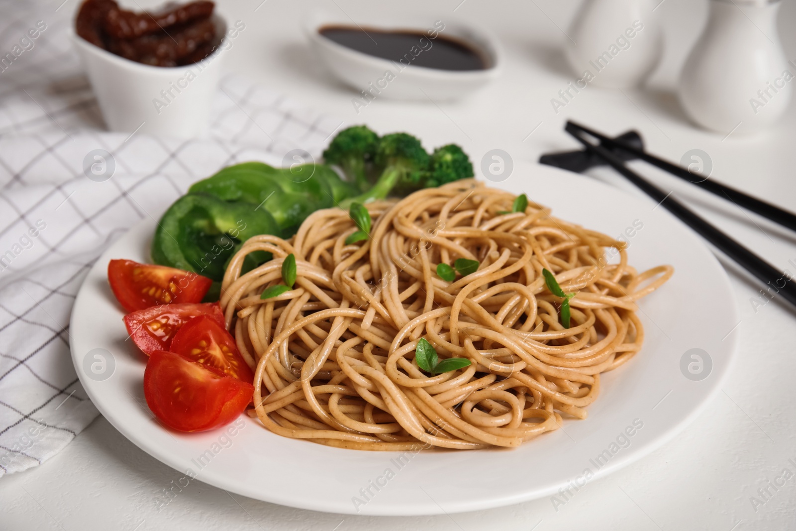 Photo of Plate of tasty buckwheat noodles with fresh vegetables on white table