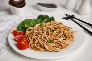 Plate of tasty buckwheat noodles with fresh vegetables on white table