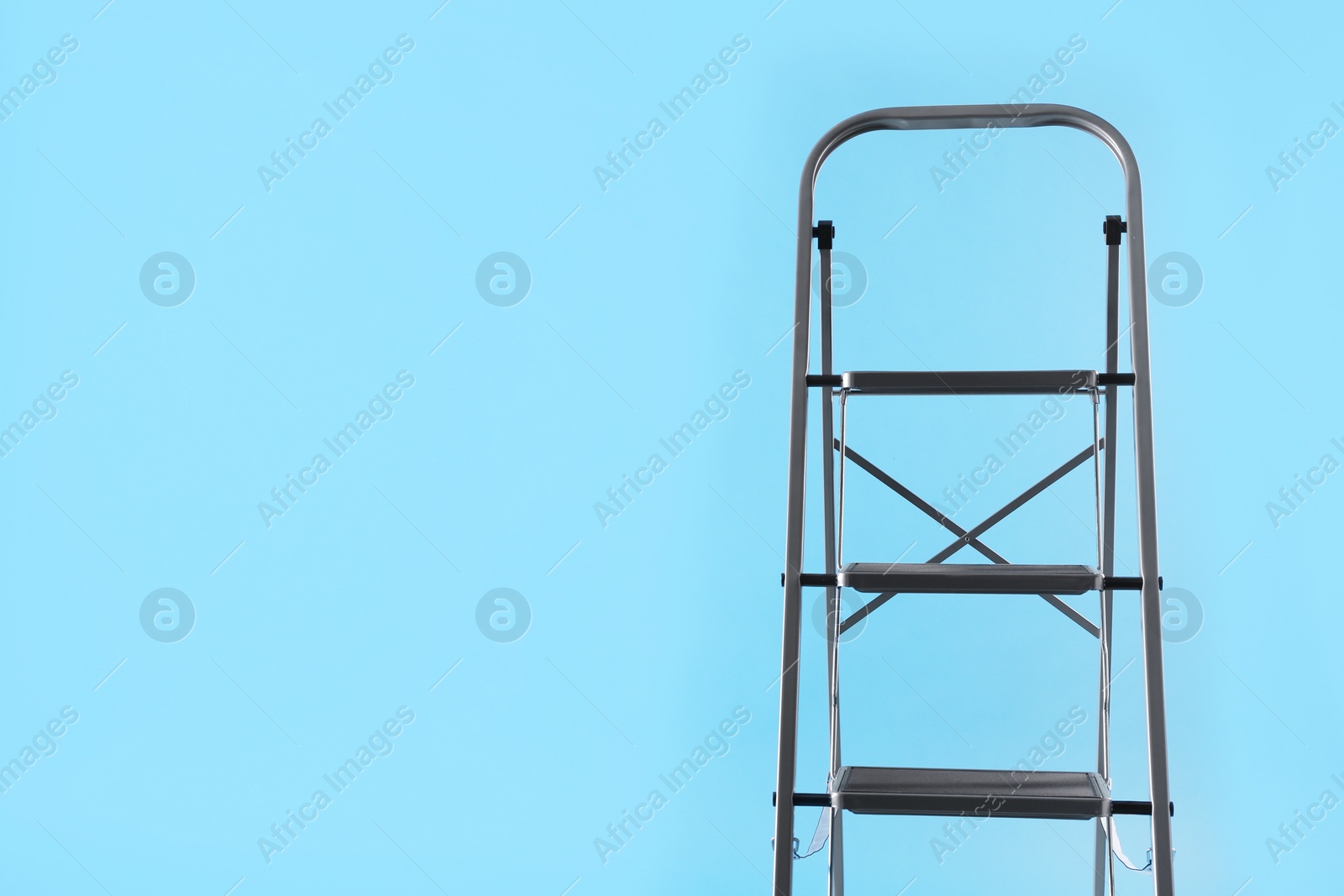 Photo of Metal stepladder on light blue background, space for text. Construction equipment