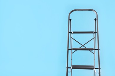 Metal stepladder on light blue background, space for text. Construction equipment