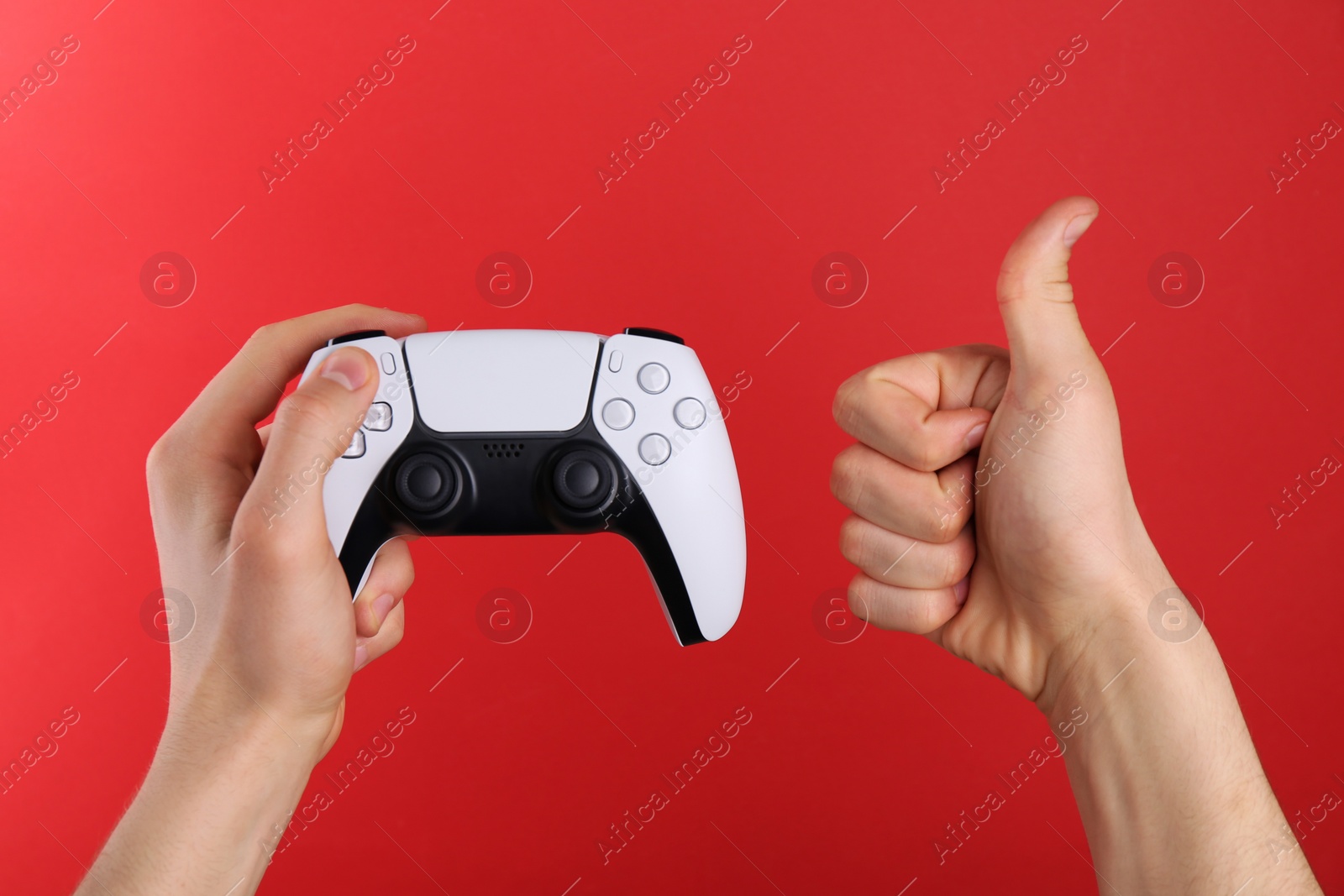 Photo of Man using wireless game controller and showing thumbs up on red background, closeup