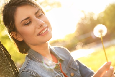 Young woman with dandelion in park on sunny day. Allergy free concept