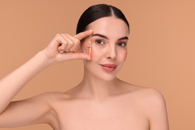 Beautiful young woman holding skincare ampoule on beige background