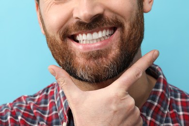 Smiling man with healthy clean teeth on light blue background, closeup