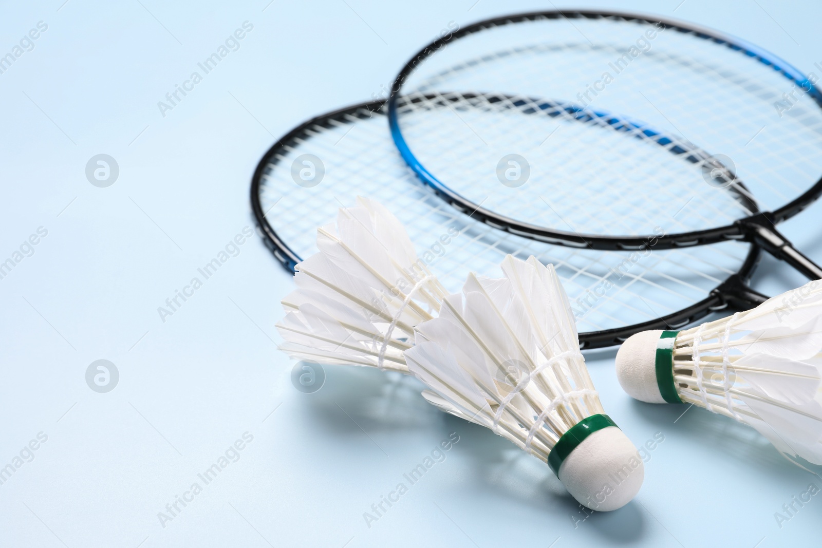 Photo of Feather badminton shuttlecocks and rackets on light blue background, closeup. Space for text